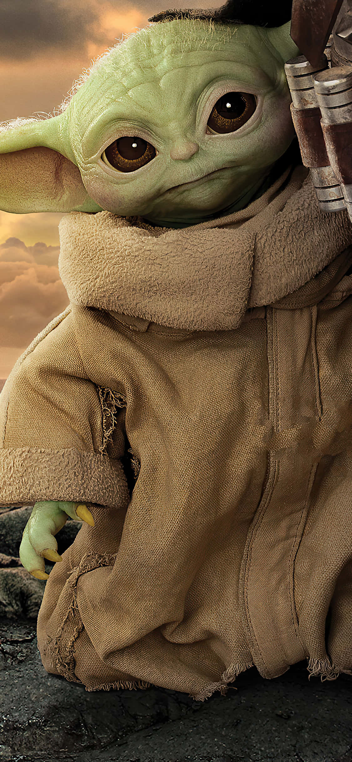 Baby Yoda iPhone 桌布 壁紙 — Grogu 身穿破舊棕色長袍的特寫，背景是戲劇性的日落天空。
