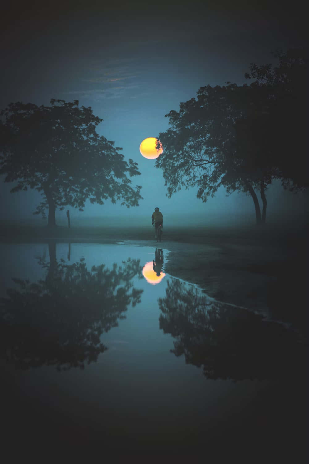  壁紙 — 一個孤獨的身影在霧夜中行走，腳下是平靜水窪中倒映的明亮滿月，兩旁是黑暗的樹木。