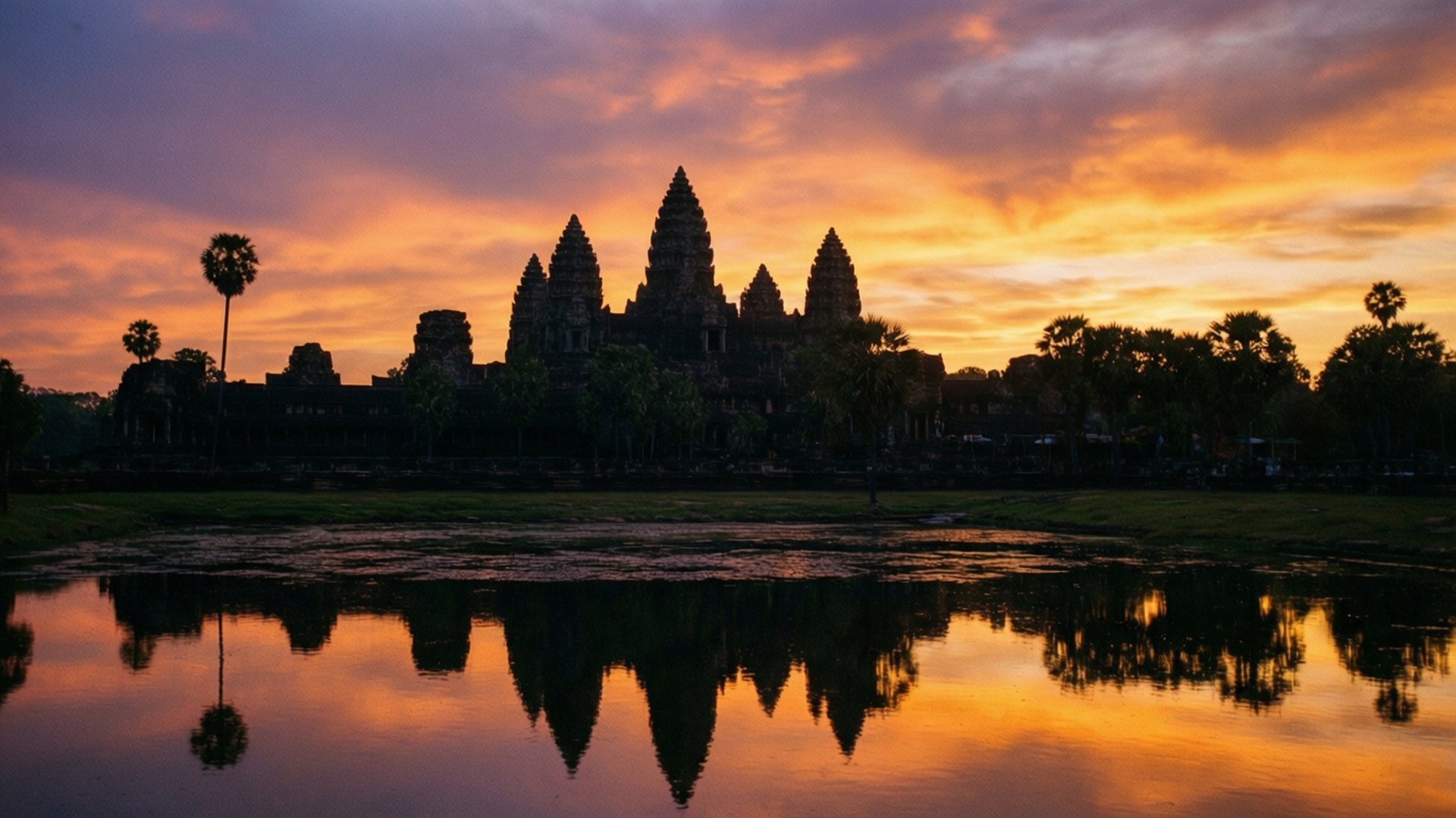 Angkor Wat Sunrise 壁紙 — 古老的吳哥窟寺廟在火紅的橙色和紫色日落映襯下形成剪影，完美倒映在平靜的水面上。