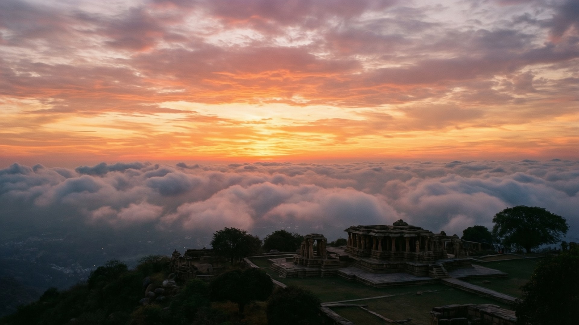 Nandi Hills Sunrise 壁紙 — 古老石廟坐落在山頂上，俯瞰著火熱橙色和粉紅色日出天空下的雲海。
