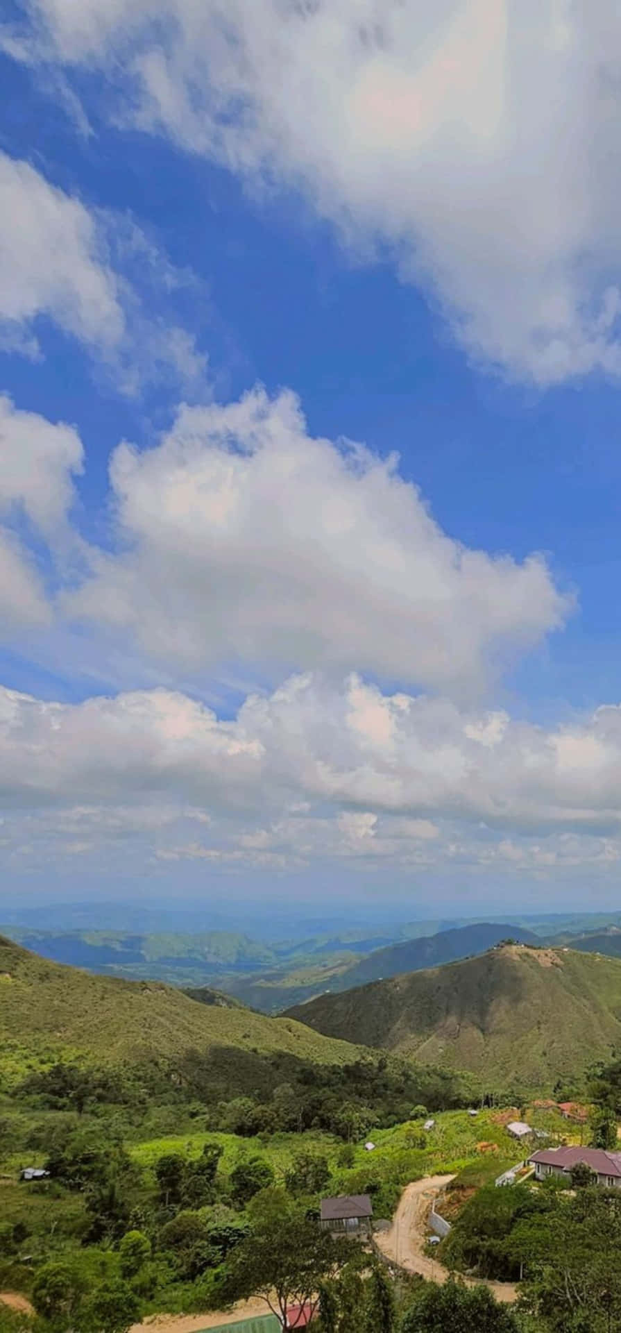  壁紙 — 廣闊的綠色山谷在點綴著蓬鬆白雲的明亮藍天下延伸。