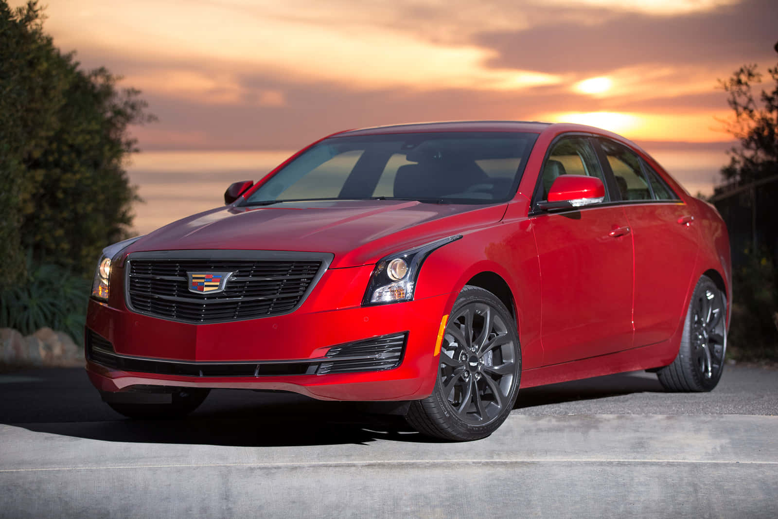 Cadillac Ats 桌布 壁紙 — 一輛光亮的紅色凱迪拉克轎車在溫暖的日落天空下閃耀，橙色雲朵和深色樹木框住場景。