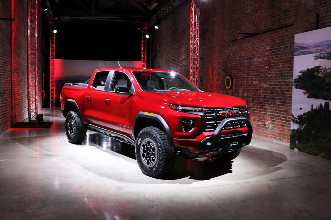 Gmc Canyon 桌布 壁紙 — 一輛光澤的紅色GMC Sierra AT4皮卡車在磚牆室內展覽空間中，在戲劇性的紅白燈光下展示。