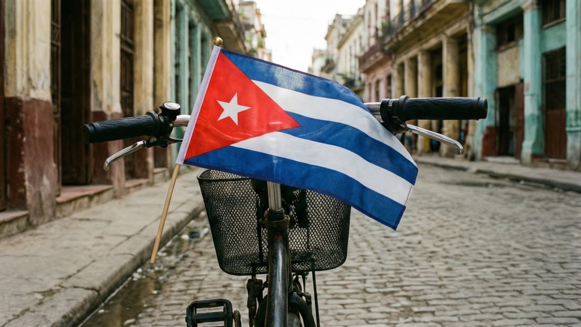 Bicycle with Flag 壁紙 — 一面古巴國旗在停放在鵝卵石街道上的自行車把手飄揚，街道兩旁是色彩繽紛的殖民建築。