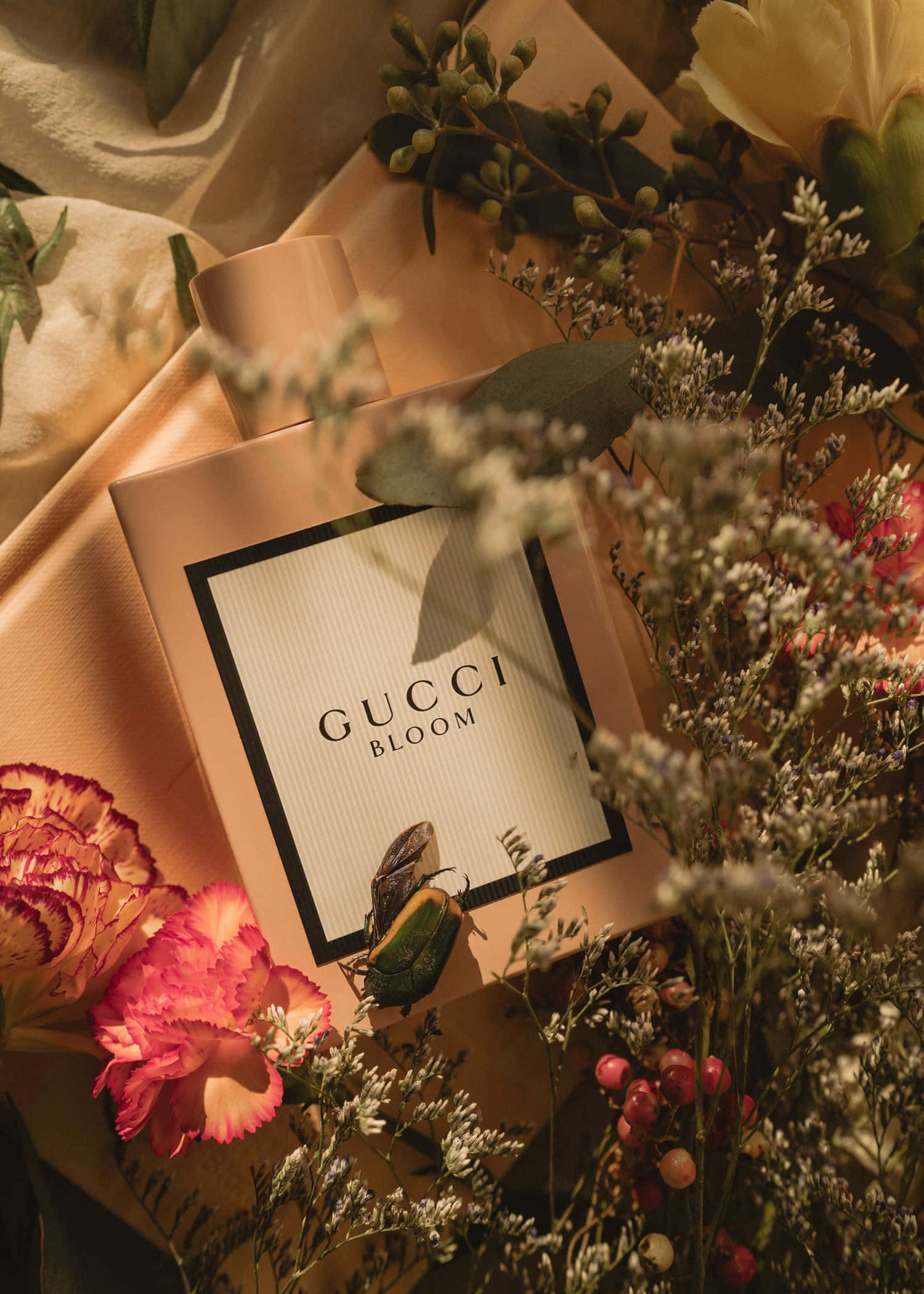 perfume 桌布 壁紙 — Gucci Bloom 香水瓶置於柔軟布料和鮮豔花朵中，沐浴在溫暖的金色光線下。