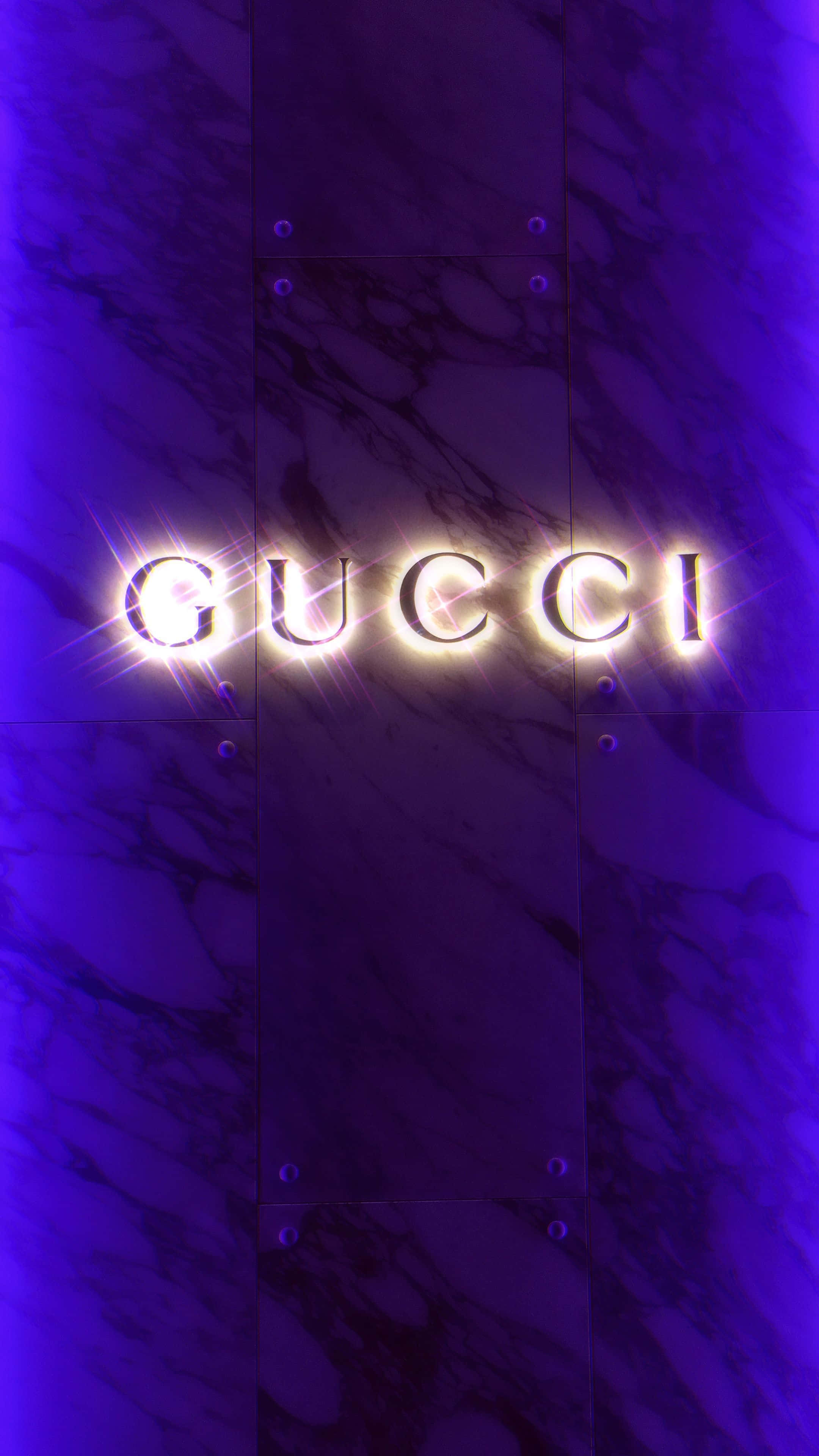 標誌 桌布 壁紙 — Gucci 標誌在深紫色大理石背景上閃爍著明亮的光芒，背景被深色面板分隔。