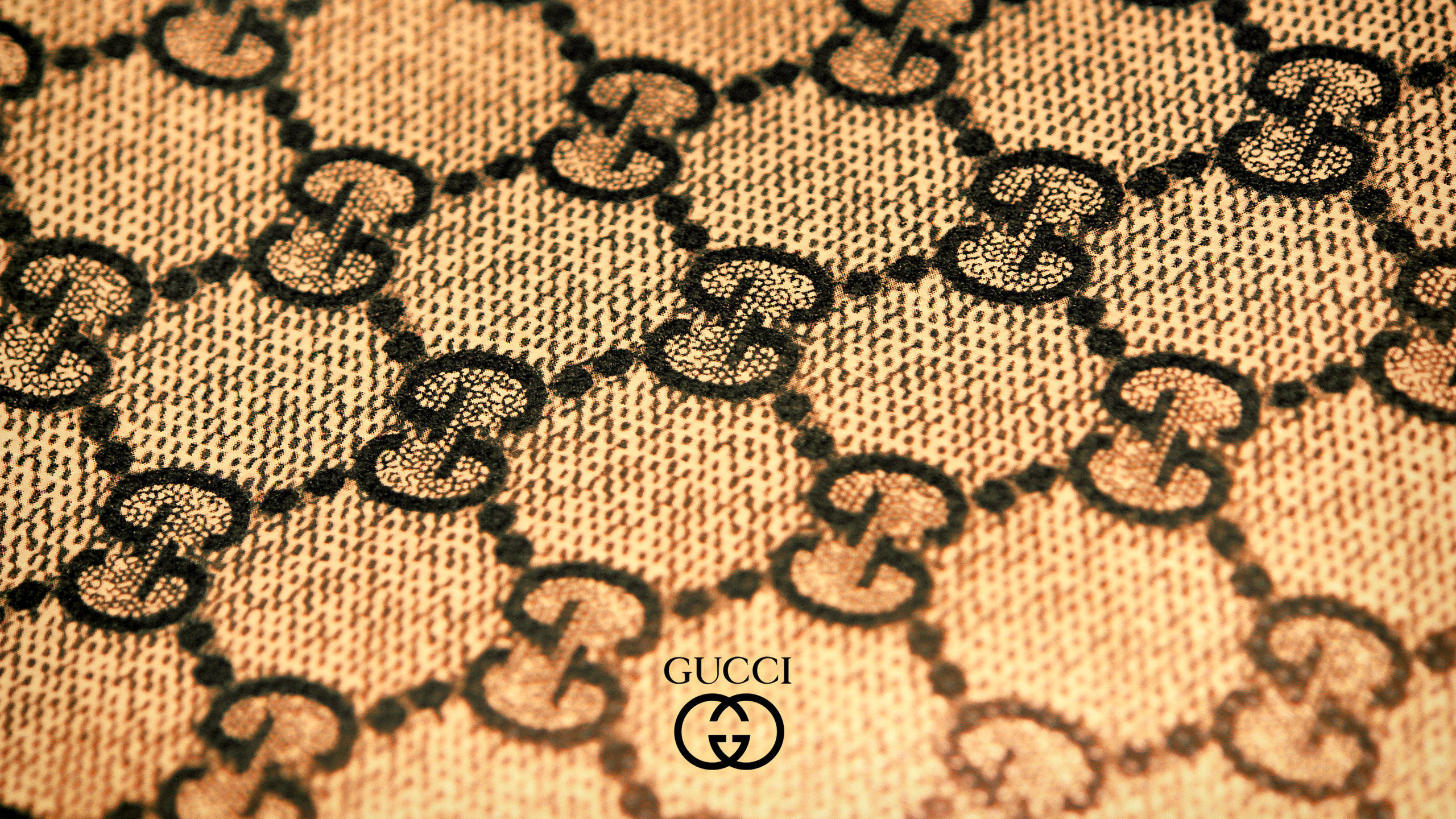 Gucci Pattern 桌布 壁紙 — Gucci 標誌性互鎖 G 字母組合圖案的特寫，呈現在帶有溫暖照明的紋理米色布料上。
