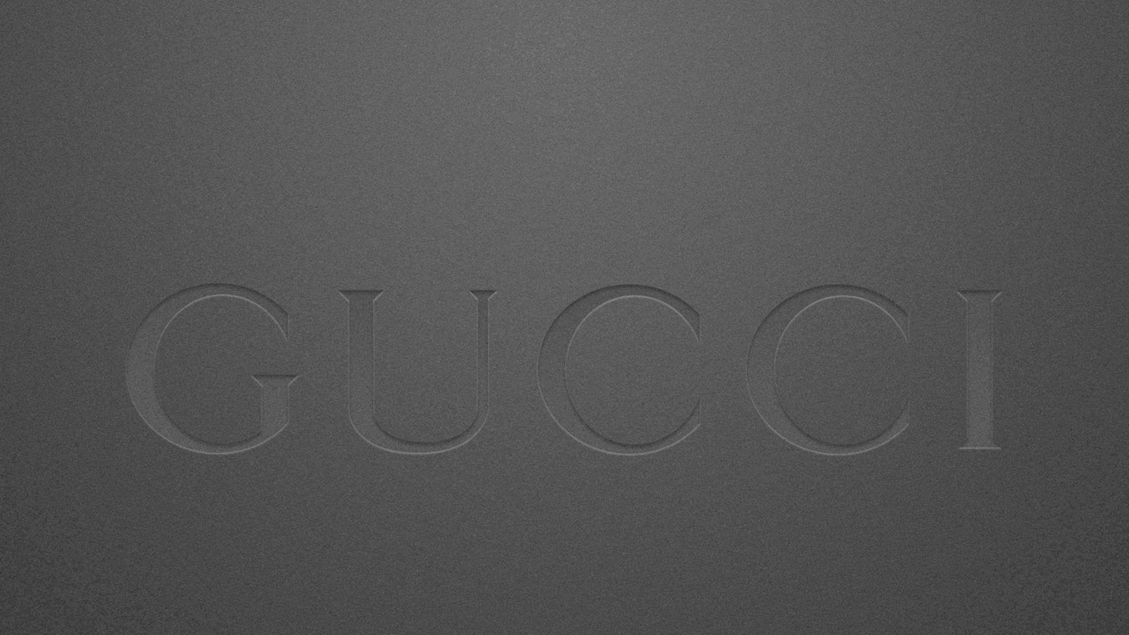Gucci 桌布 壁紙 — GUCCI 這個字以極簡的單色風格微妙地壓印在有紋理的深灰色表面上。