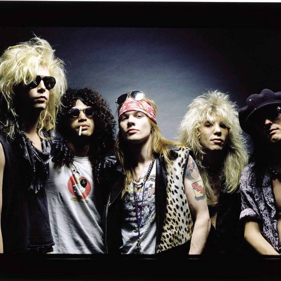 攝影 桌布 壁紙 — Guns N' Roses 樂團成員以狂野的頭髮、太陽眼鏡和皮背心在黑暗的錄音室背景下擺姿勢。