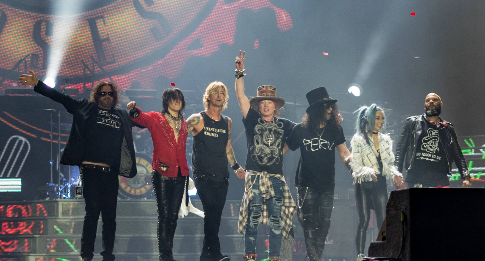 guns n roses 桌布 壁紙 — Guns N' Roses 樂團成員在煙霧和聚光燈下，於燈光璀璨的演唱會舞台上充滿活力地擺出姿勢。