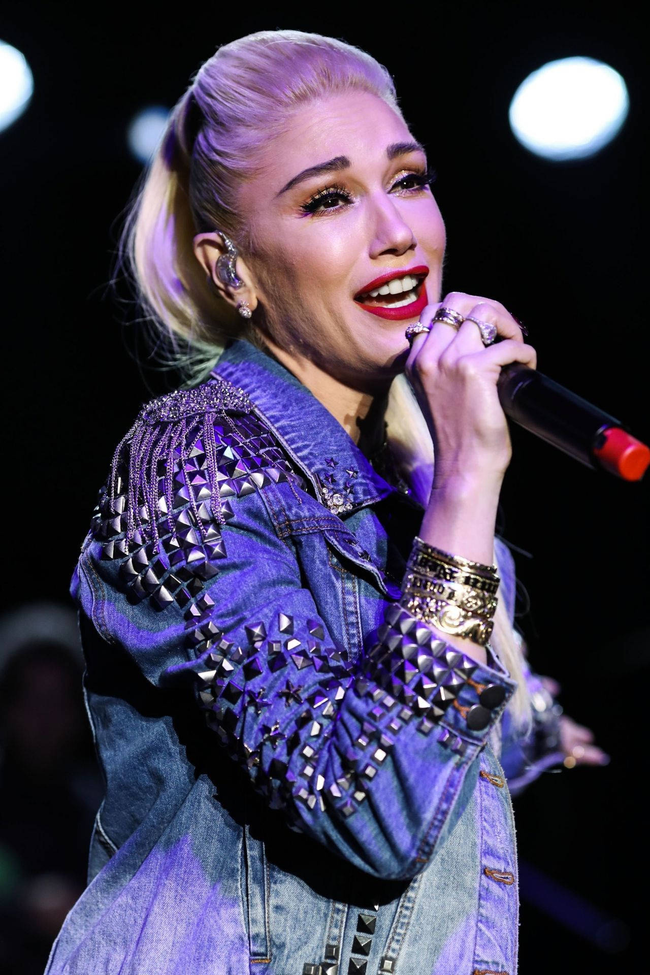 Stefani 桌布 壁紙 — Gwen Stefani 在明亮的舞台燈光下，穿著飾有鉚釘的牛仔外套，熱情地在台上演唱。