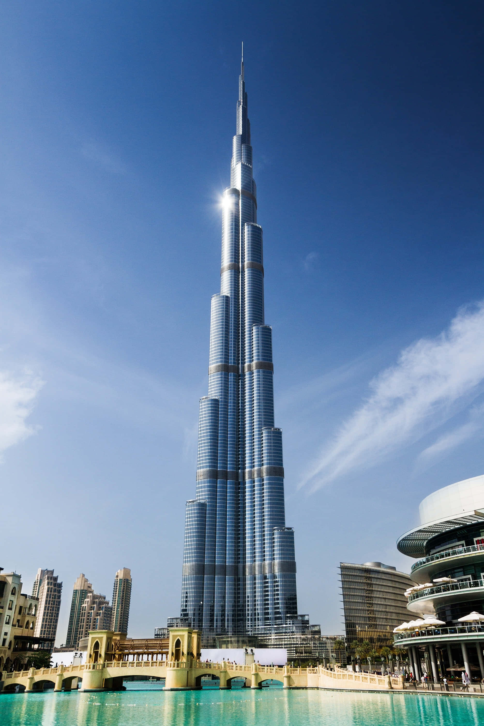 Burj Khalifa 桌布 壁紙 — 哈里發塔在清澈藍天和縷縷白雲下，聳立於碧綠色的泳池之上。