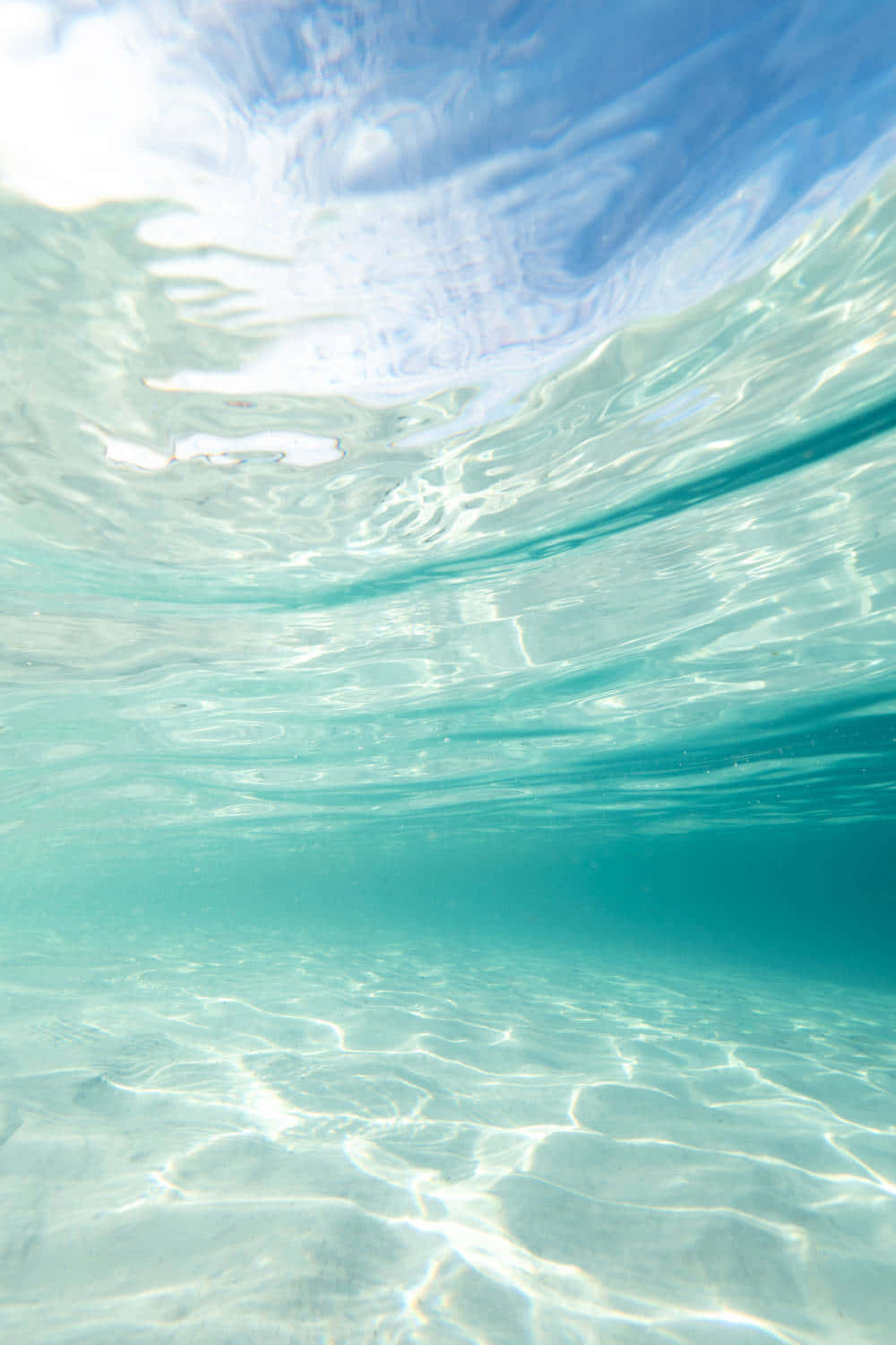  壁紙 — 海底景觀，呈現碧綠海洋，陽光漣漪在沙質海底上舞動，並倒映著藍天。