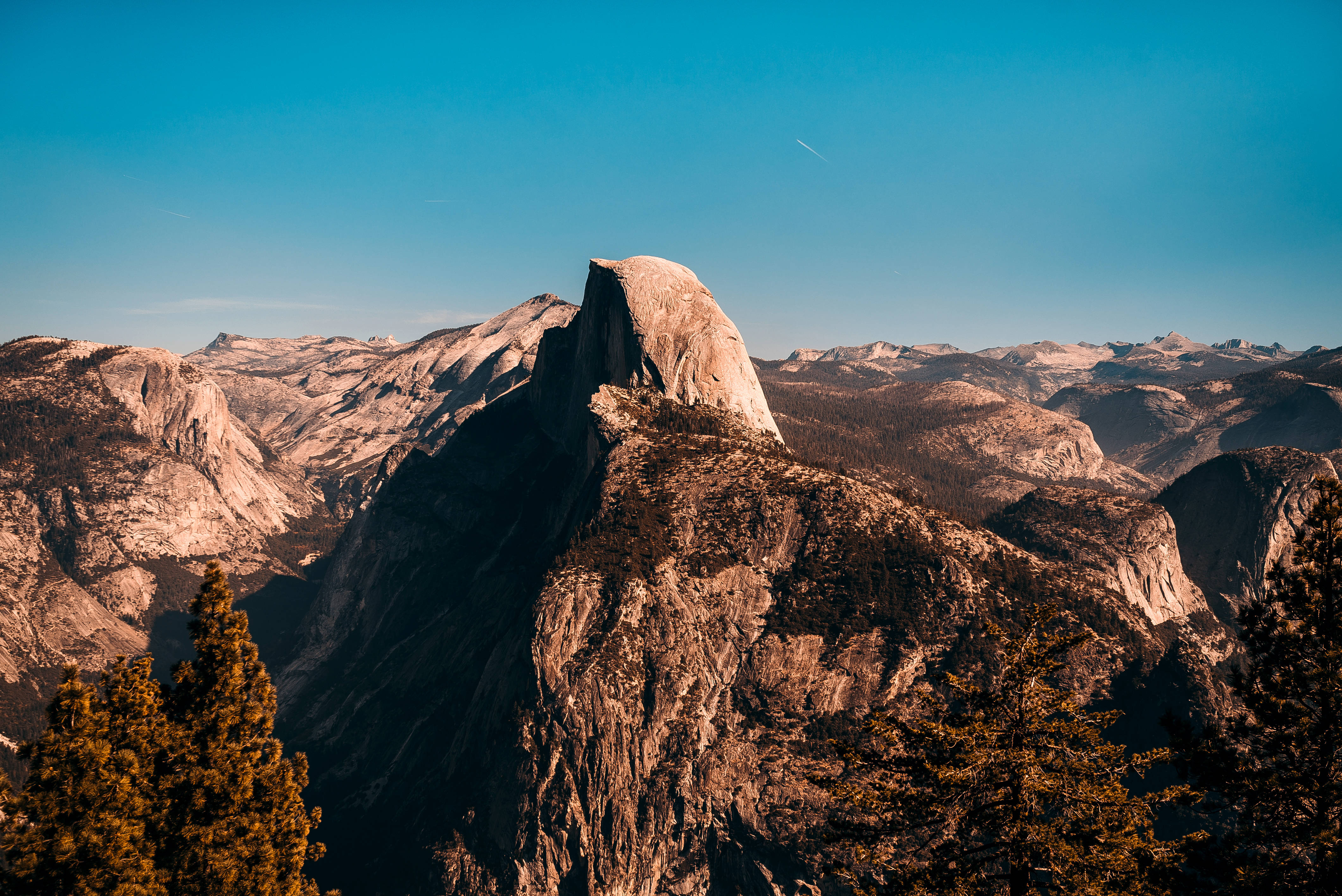 超酷的動圖 桌布 壁紙 — Half Dome 雄偉地聳立在清澈的藍天下，金色的陽光照射在其花崗岩表面和周圍的山脈上。