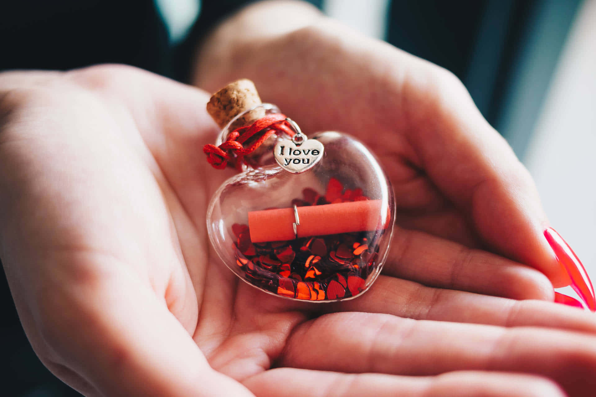  壁紙 — 一隻手捧著一個心形玻璃瓶，裡面裝滿紅色亮粉和一卷寫著「我愛你」的字條。