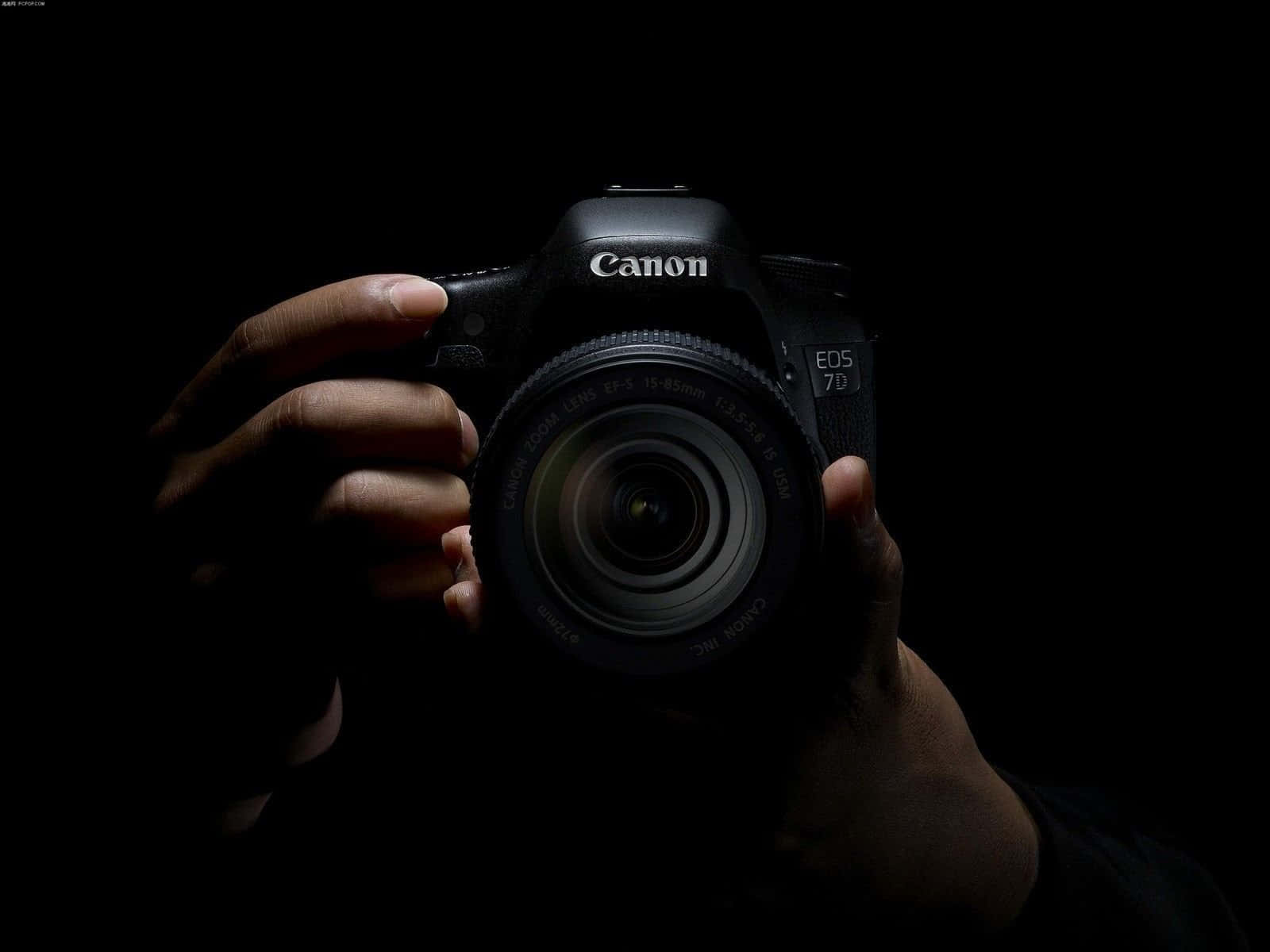 Cameraman 桌布 壁紙 — 一隻手在純黑色背景上，以戲劇性的聚光燈照射下，拿著一台黑色的Canon EOS 7D DSLR相機。