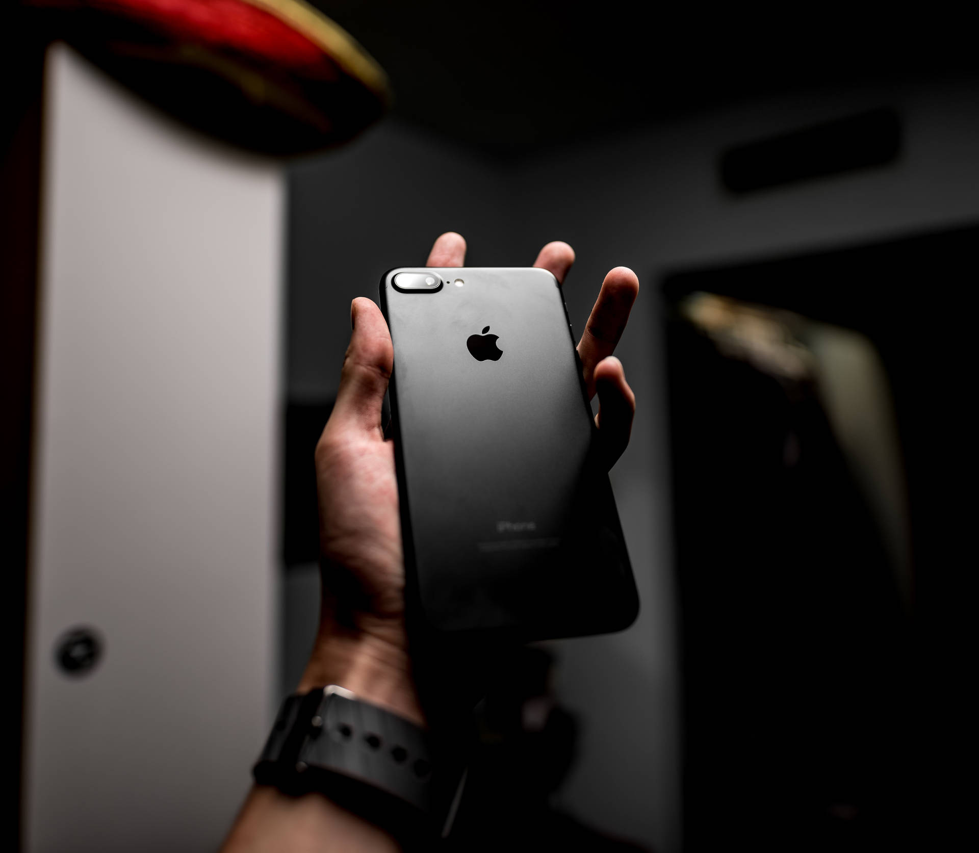 手在昏暗燈光下拿著帶有Apple標誌的黑色iPhone。 — iPhone 11 壁紙