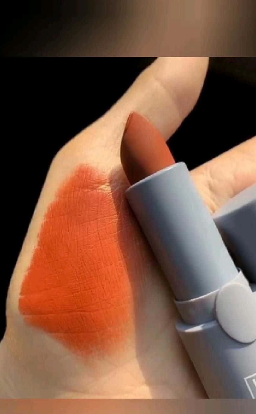 lipstick 桌布 壁紙 — 一隻手拿著一支霧面橙色唇膏，在手背上大膽地試色，背景為深色。