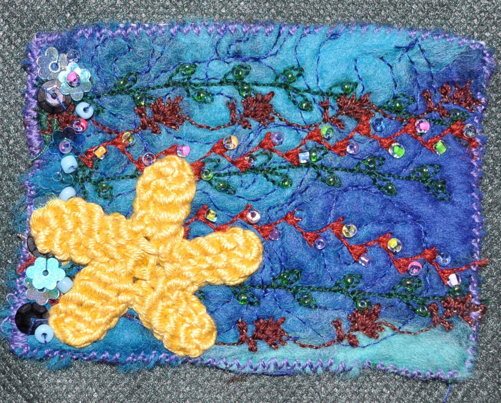 手工紡織品，帶有鉤針編織海星和珠子藤蔓，置於藍色布料上。 — Stitch 壁紙