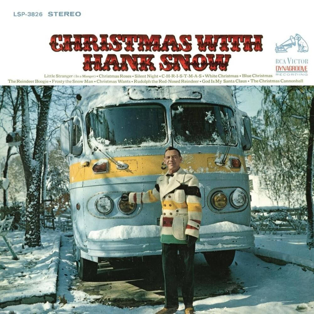 音樂 桌布 壁紙 — Hank Snow 在明亮的冬日陽光下，站在一個被雪覆蓋的復古巴士旁邊的雪地庭院中微笑。
