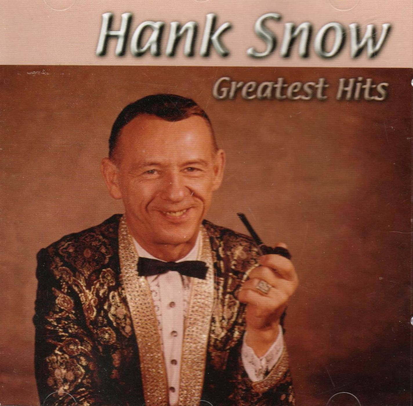 音樂 桌布 壁紙 — Hank Snow 穿著閃閃發光的金色和黑色外套，拿著煙斗，在棕色工作室背景前溫暖地微笑。