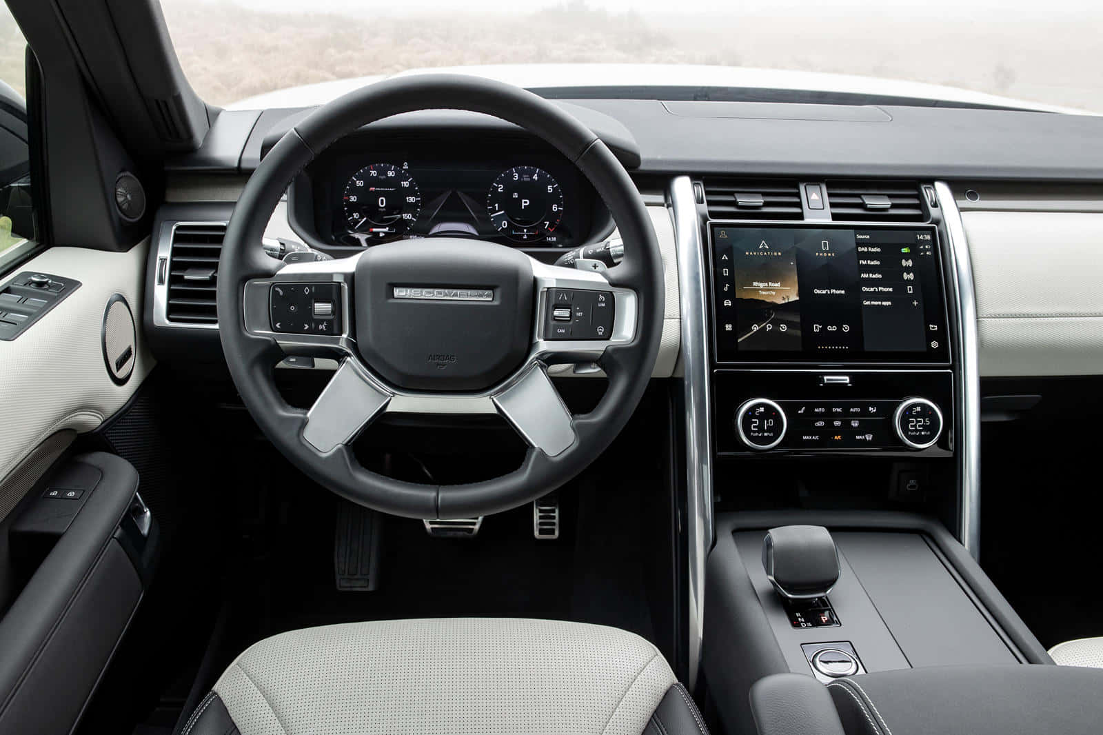 Land Rover Discovery 桌布 壁紙 — 豪華SUV內裝，黑色方向盤搭配銀色飾條，數位儀表板顯示車輛控制和空調設定。