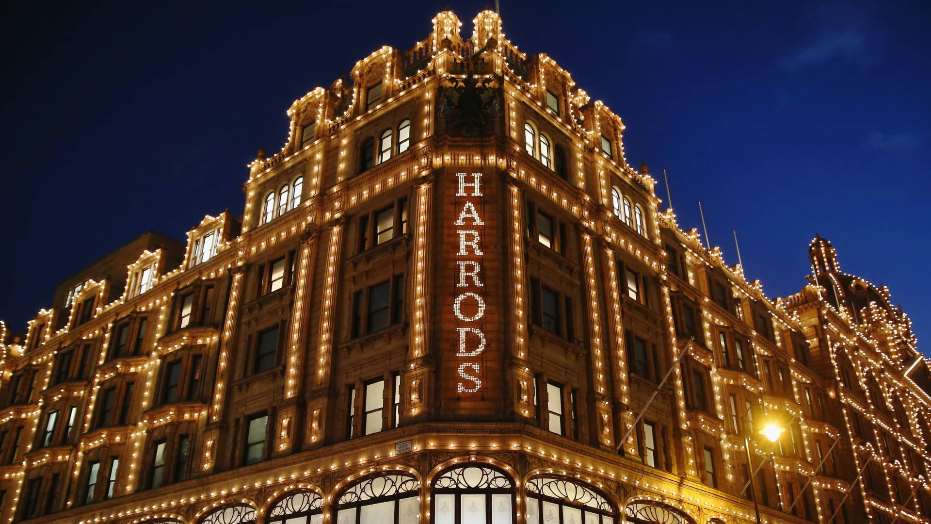 Blue Sky 桌布 壁紙 — Harrods 百貨公司在深藍色的夜空下溫暖地發光，其華麗的外牆裝飾著閃爍的燈串。