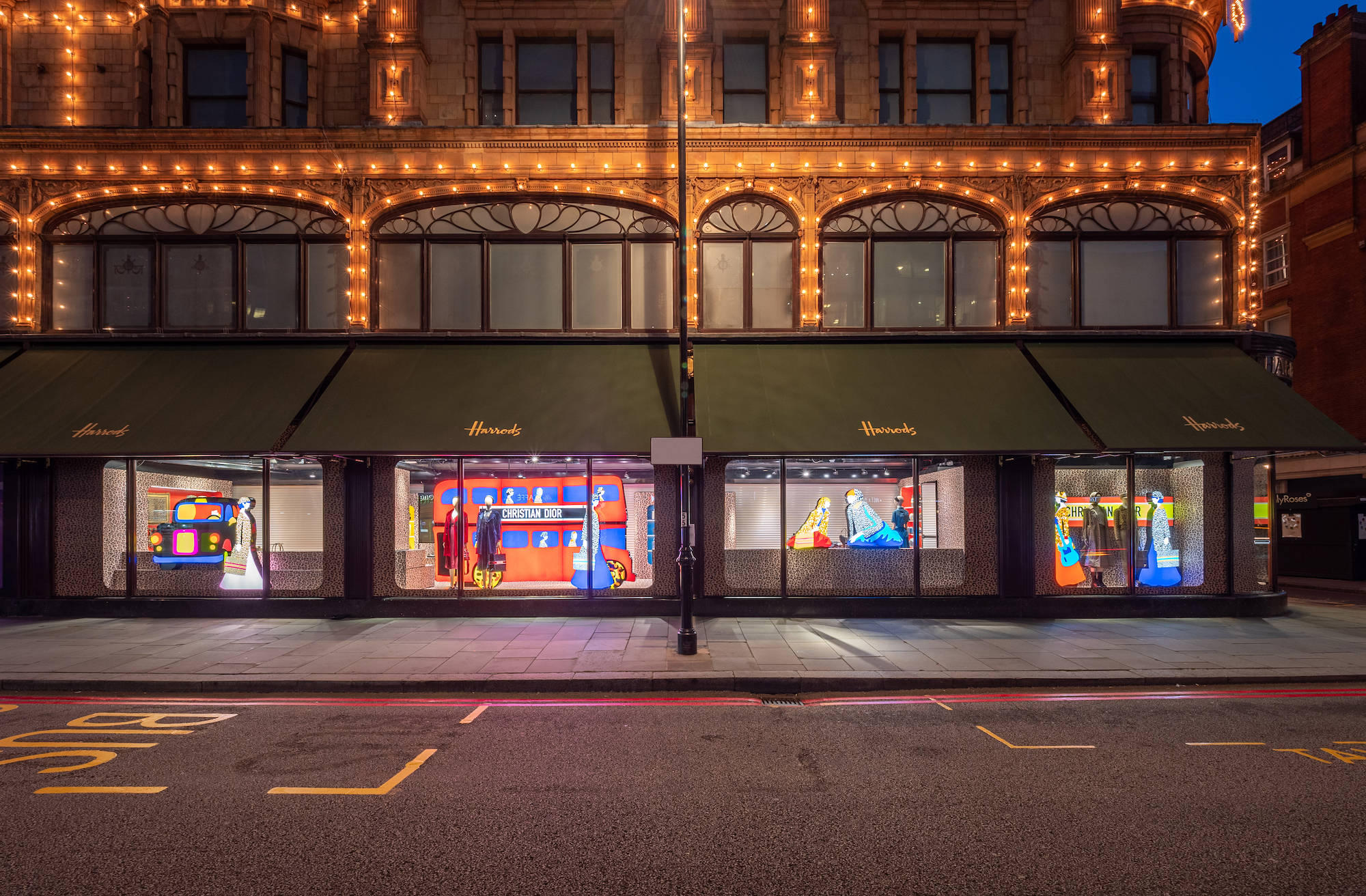 Shopping 桌布 壁紙 — Harrods 百貨公司外牆在黃昏時分，溫暖的串燈在色彩繽紛的櫥窗展示上方閃爍。