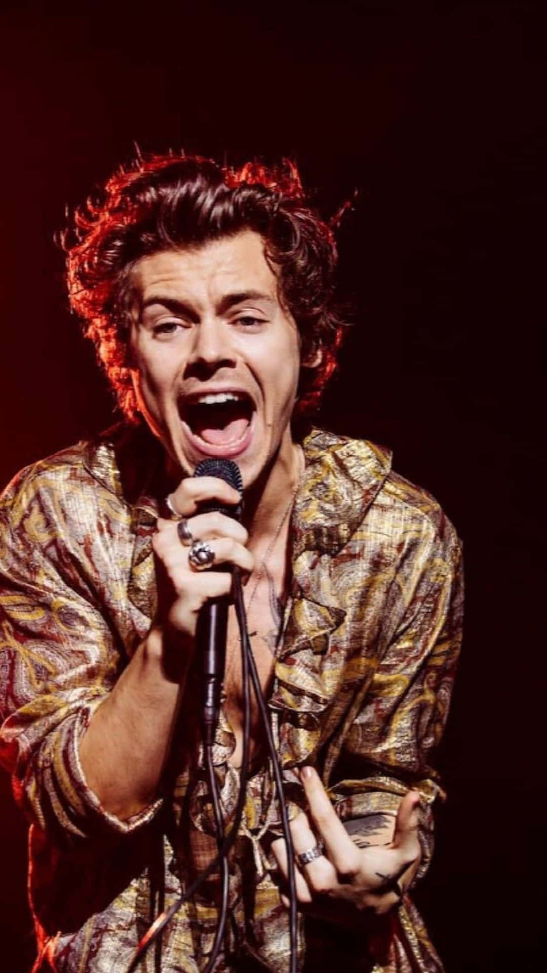 哈利·史泰爾斯 桌布 壁紙 — Harry Styles 在戲劇性的紅色舞台燈光下，頭髮蓬亂，熱情地對著麥克風唱歌。