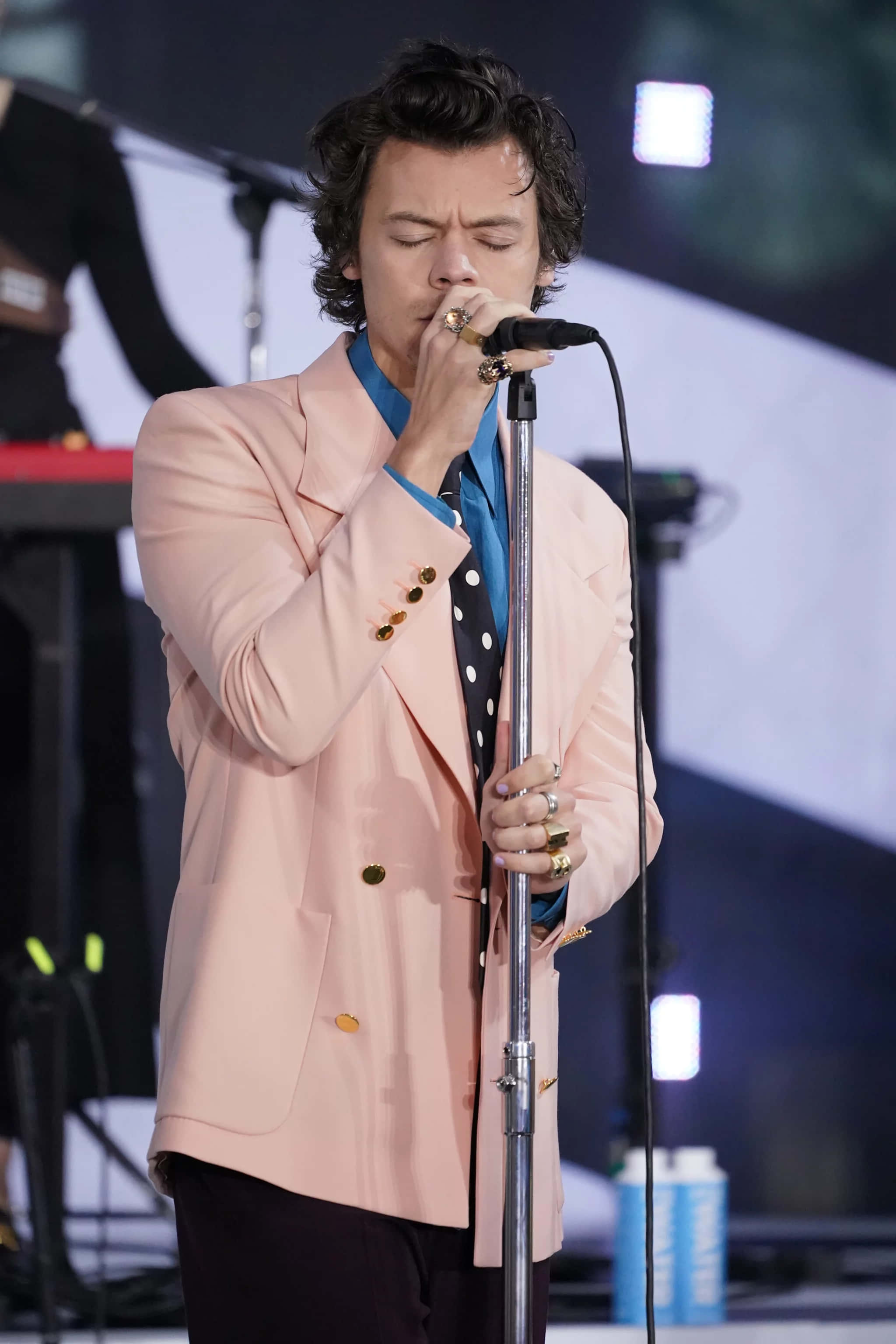 Harry Styles 2021 桌布 壁紙 — Harry Styles 在舞台上穿著粉紅色西裝外套和波點襯衫，熱情地對著麥克風唱歌。