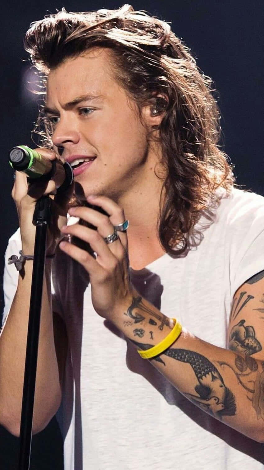 哈利·史泰爾斯 桌布 壁紙 — Harry Styles 在舞台燈光下，手臂上的刺青清晰可見，深情地對著麥克風唱歌。