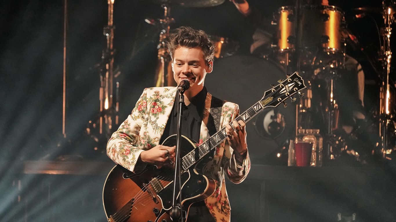 Harry Styles Laptop 桌布 壁紙 — Harry Styles 穿著花卉西裝外套，在戲劇性的舞台燈光下拿著吉他表演。