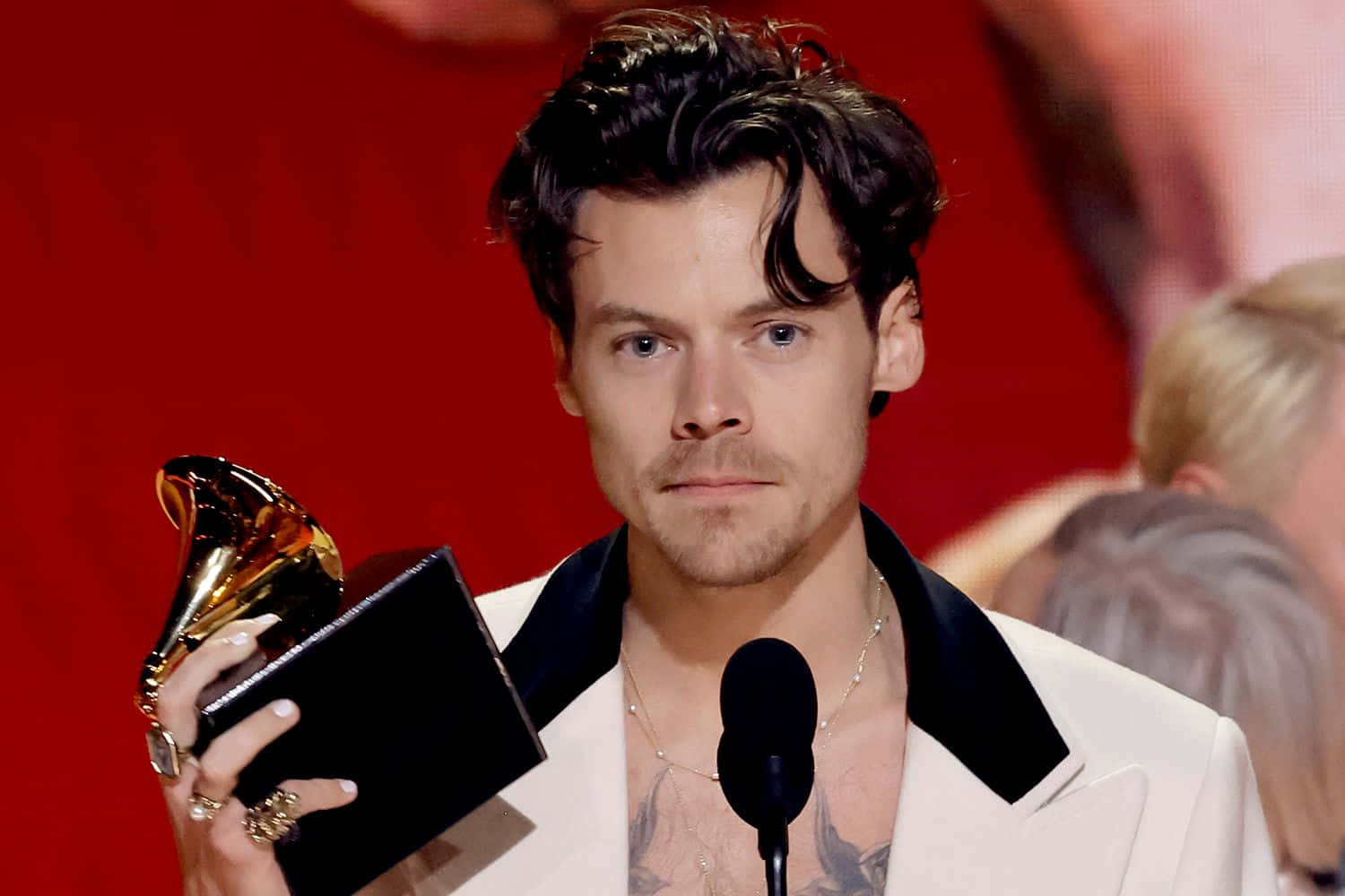 Harry Styles 2021 桌布 壁紙 — Harry Styles 身穿白色西裝，在紅色背景下於舞台上手持葛萊美獎。
