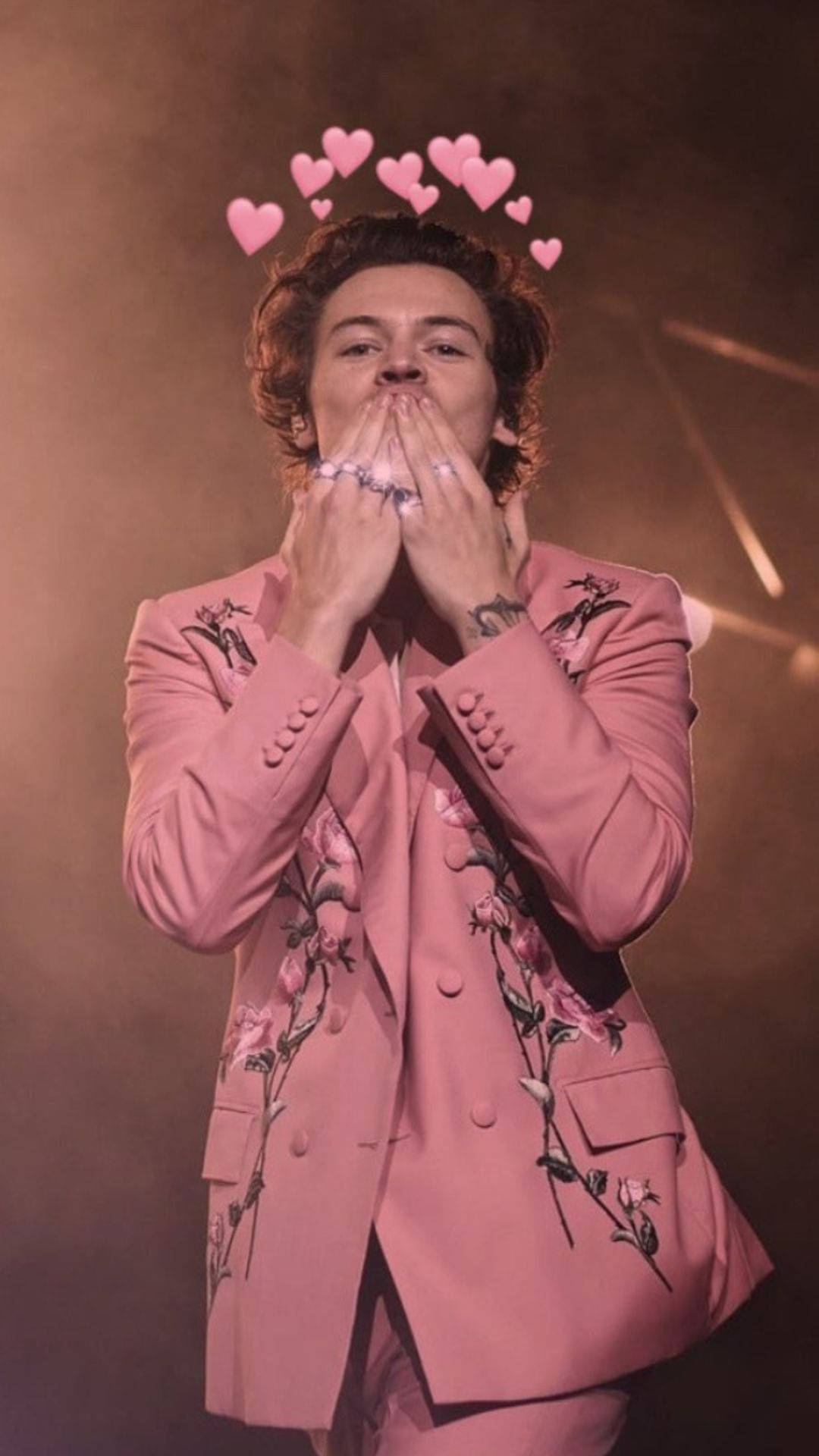 哈利·史泰爾斯 桌布 壁紙 — Harry Styles 身穿粉紅色花卉西裝，在舞台燈光下飛吻，頭頂有漂浮的心形。