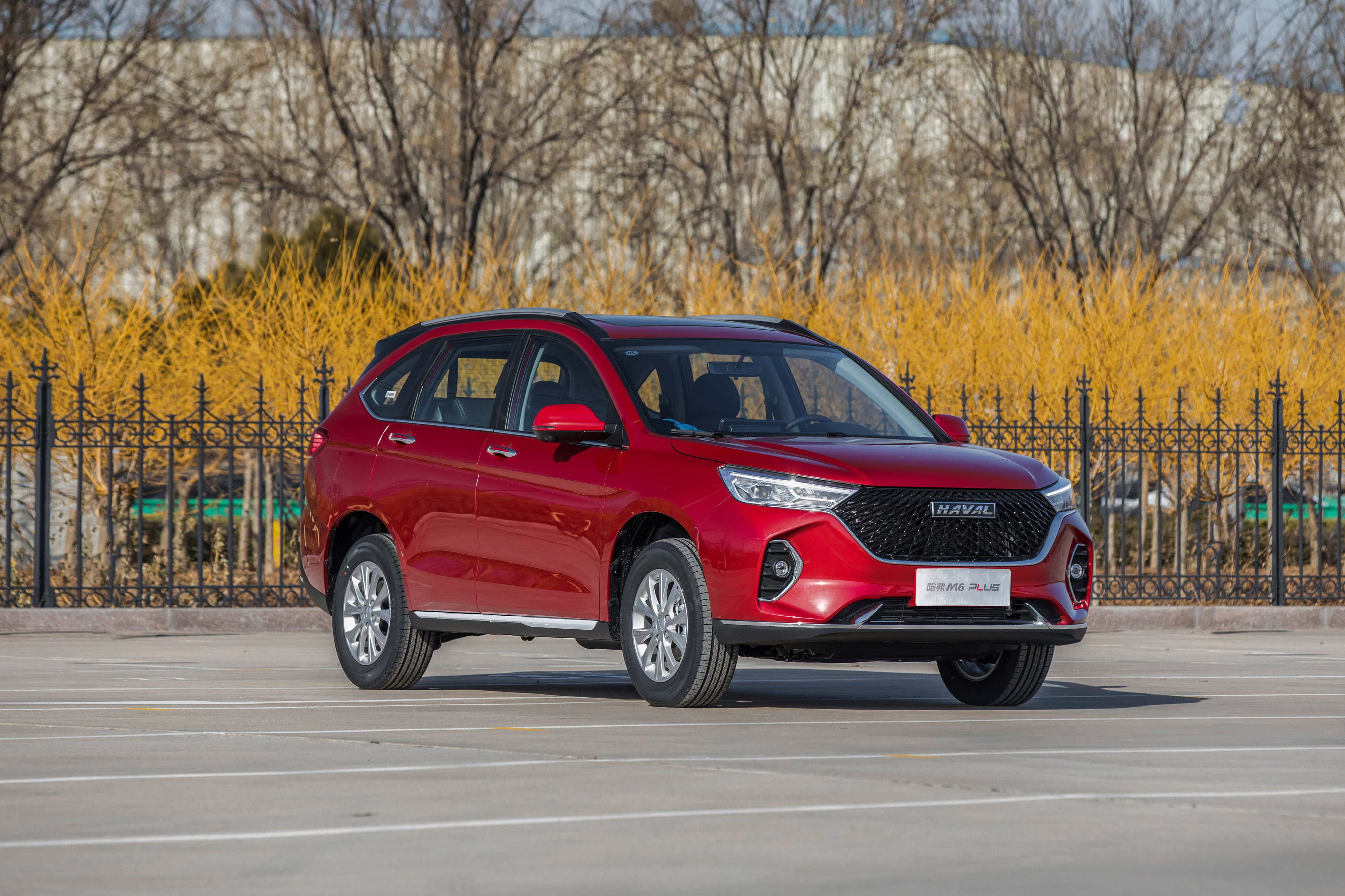 Haval SUV 行駛於美麗山景中 壁紙 — 一輛亮面紅色哈弗SUV停在瀝青路上，黑色圍欄後面有光禿禿的樹木和金色灌木，在晴朗的日光下。