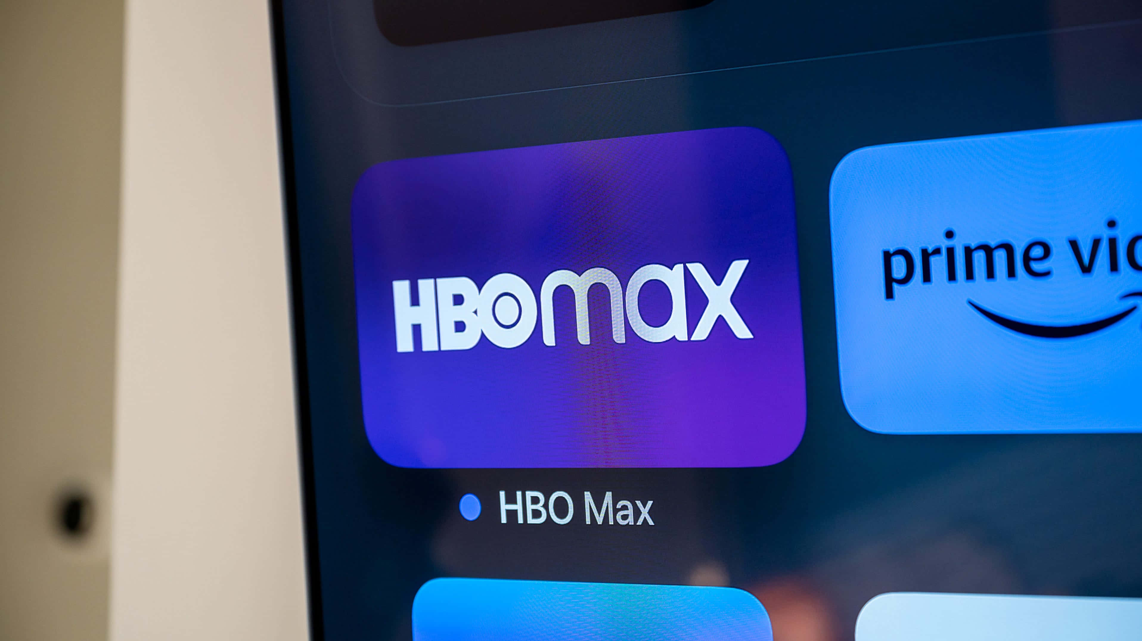 HBO 桌布 壁紙 — HBO Max 應用程式圖示在串流服務主畫面上發出紫色光芒的特寫，旁邊可見 Prime Video。