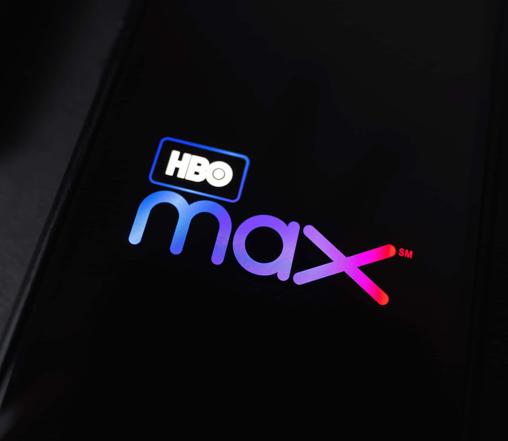 HBO 桌布 壁紙 — HBO Max 標誌在深色智慧型手機螢幕上發出從藍色到粉紅色的漸變光芒。