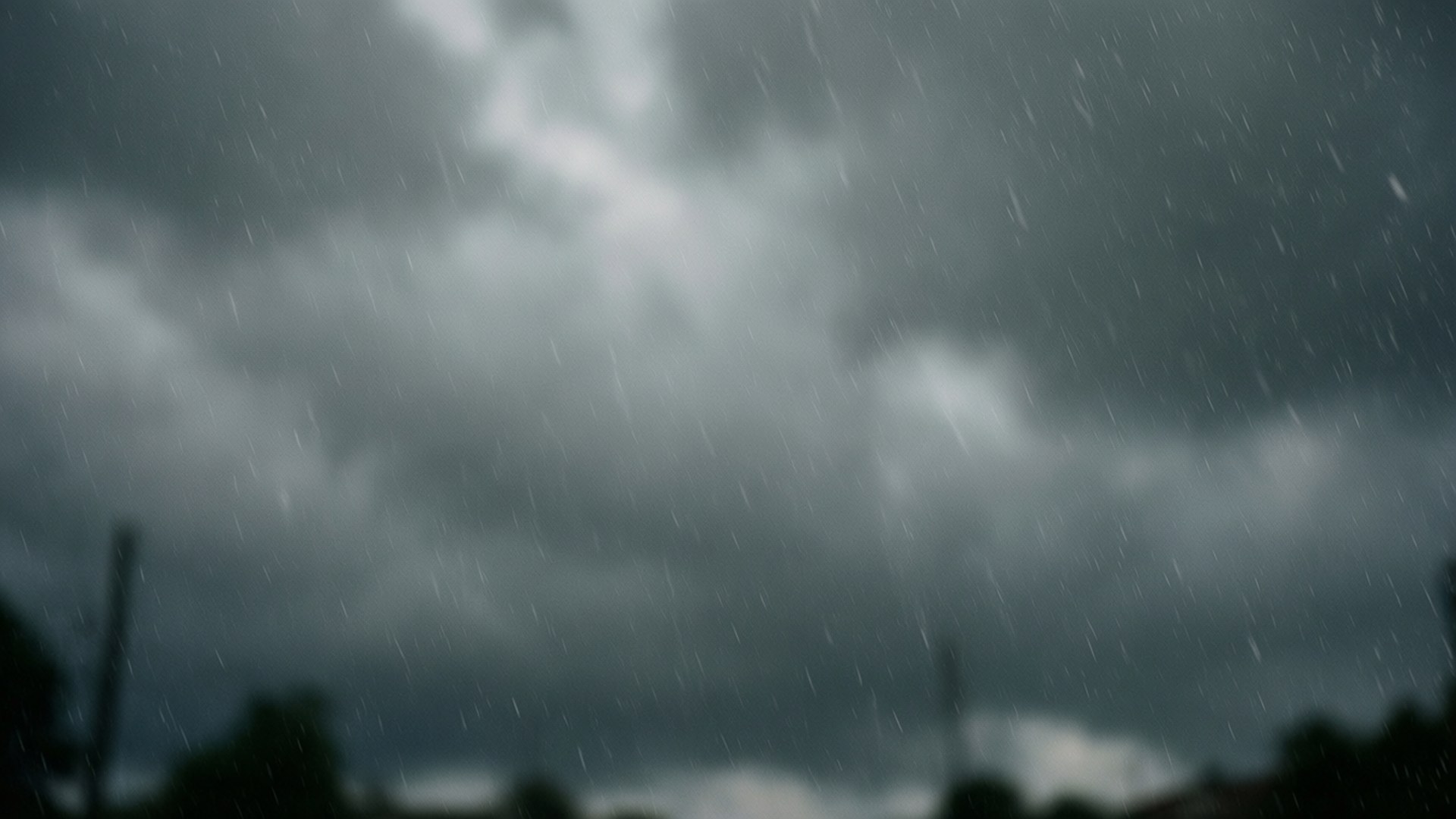 Moody Rainy Sky 壁紙 — 大雨如注，劃過佈滿陰沉烏雲的深灰色天空，下方是模糊的樹木剪影。