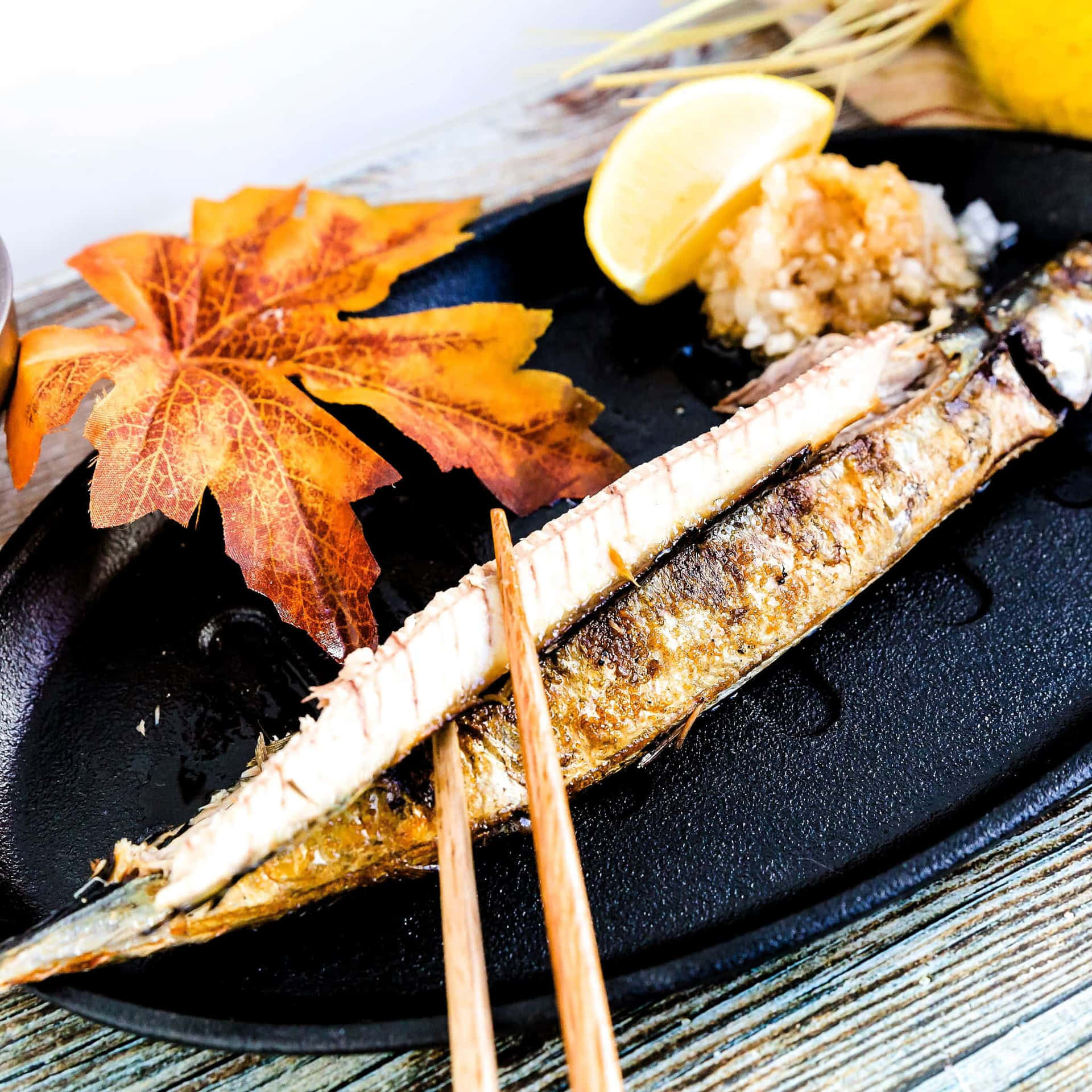  壁紙 — 黑盤上的烤魚配筷子和秋葉，附檸檬和米飯。