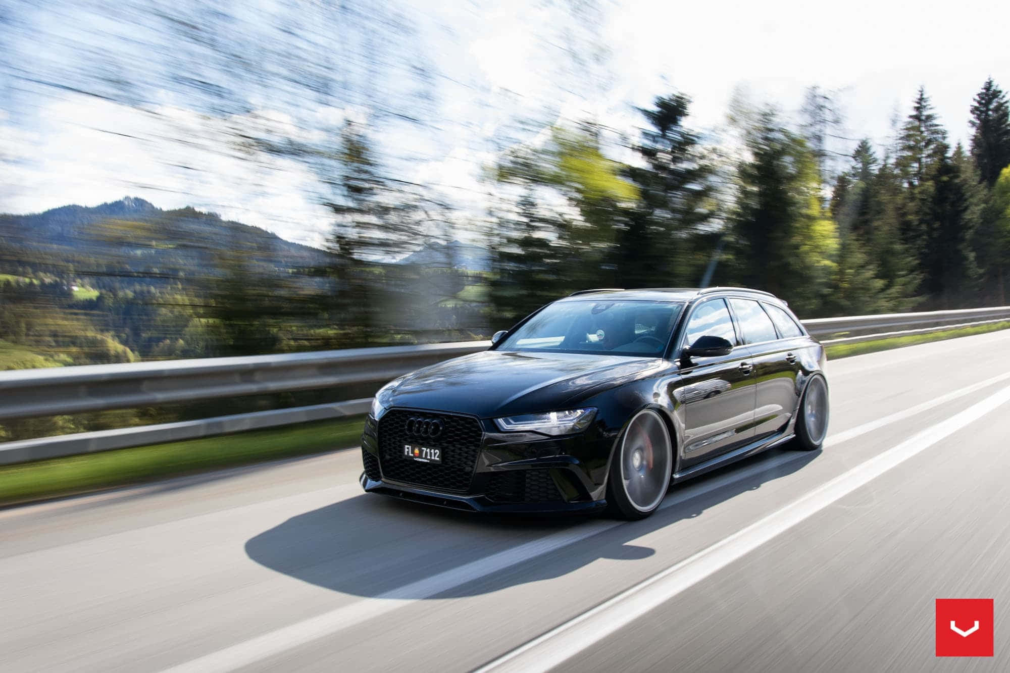 Audi Rs6 桌布 壁紙 — 一輛時尚的黑色奧迪RS6 Avant在陽光普照的山區高速公路上飛馳，模糊的綠色樹木和山丘從旁掠過。