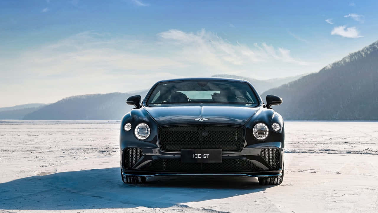 Bentley Continental Gt 桌布 壁紙 — 一輛時尚的黑色Bentley ICE GT停放在廣闊的雪原上，背景是白雪覆蓋的山脈，天空清澈湛藍。