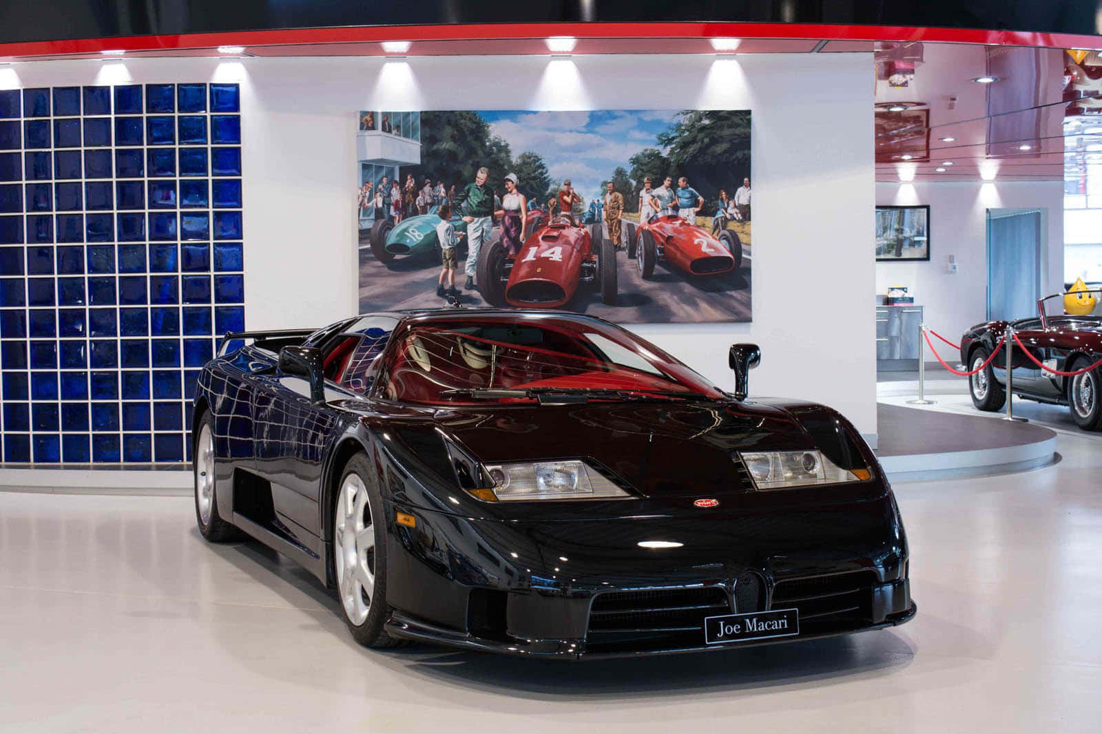 Bugatti Eb110 桌布 壁紙 — 一輛時尚的黑色Bugatti跑車在現代博物館中，在明亮的燈光下閃閃發光，博物館有藍色玻璃牆和復古賽車海報。