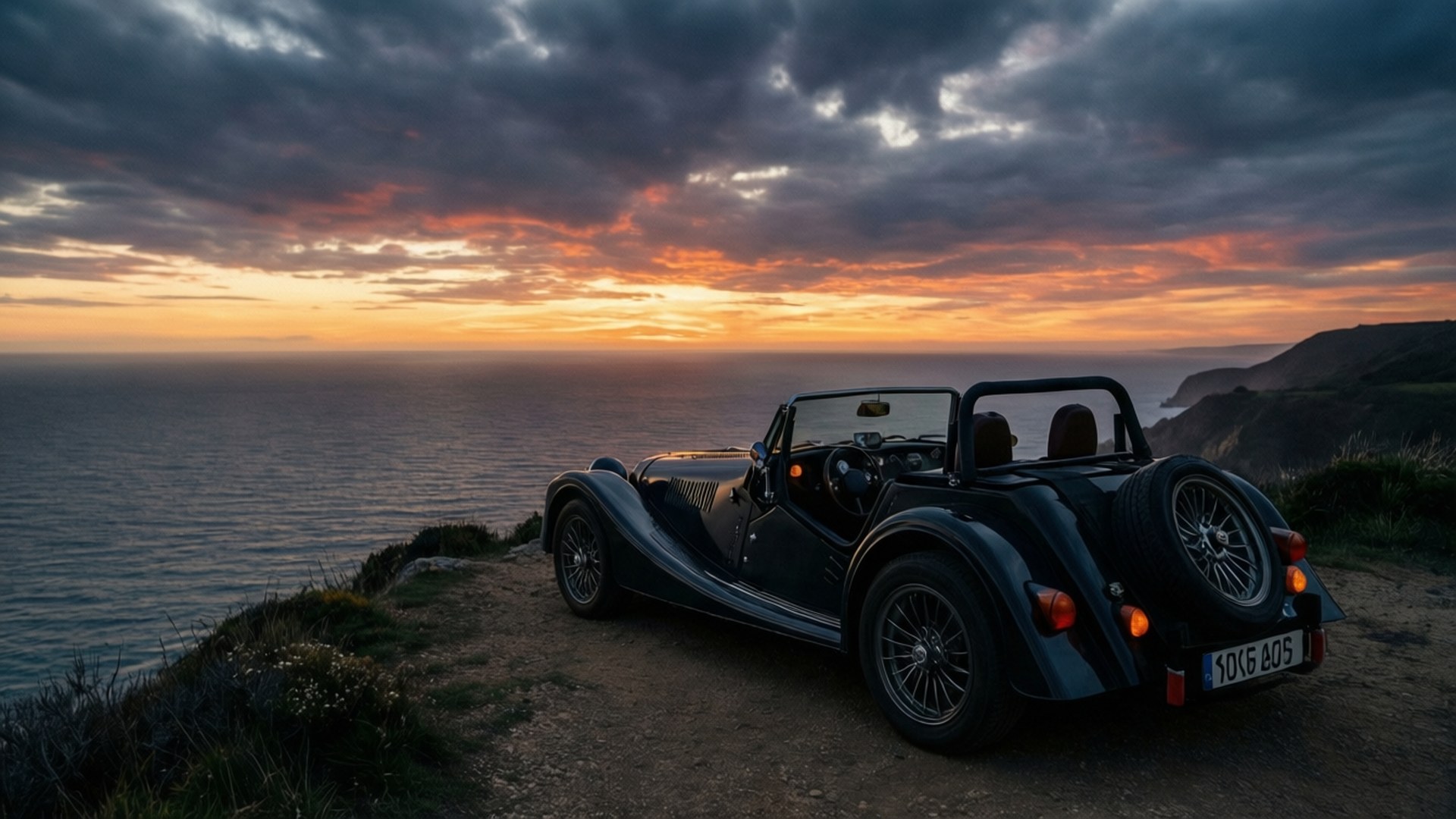 Morgan Roadster 桌布 壁紙 — 一架時尚的黑色敞篷跑車停泊在懸崖邊，俯瞰日落時分的海洋，天空中有火橙色和紫色的雲彩。