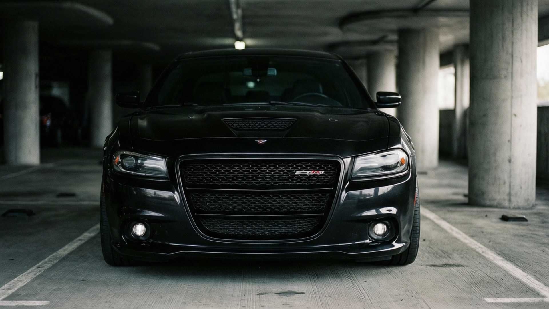 Garage SRT8 壁紙 — 一輛時尚的黑色Dodge Challenger SRT8在昏暗的混凝土停車場中向前，有柱子和褪色線條。