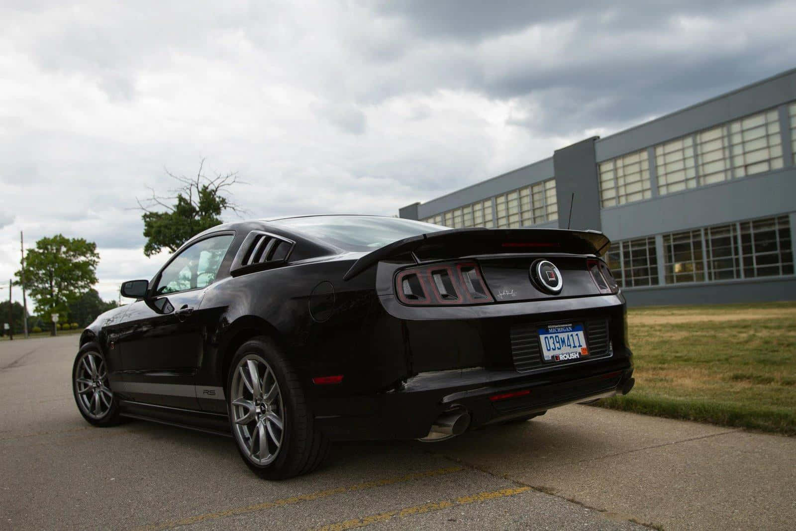 Ford Mustang Roush 桌布 壁紙 — 一輛時尚的黑色福特Mustang GT停在鋪砌的停車場，天空多雲，背景有現代建築。