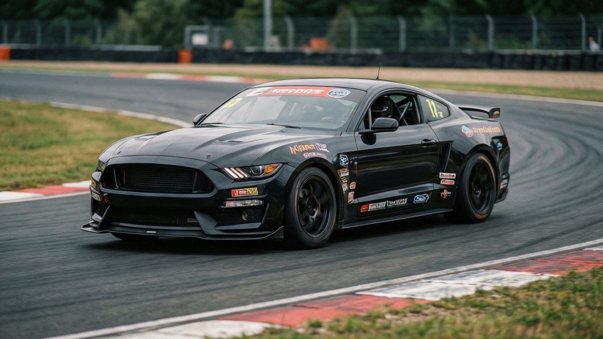 GTD Track Attack 壁紙 — 一輛帶有贊助商貼紙的黑色福特野馬賽車在賽道彎道上高速行駛，彎道有紅白路緣石。