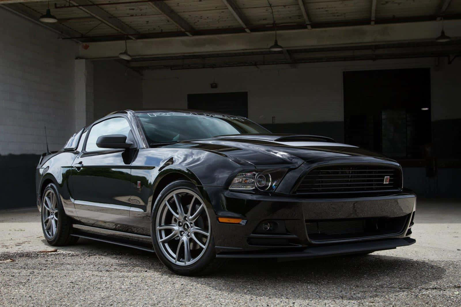 Ford Mustang Roush 桌布 壁紙 — 一輛時尚的黑色福特野馬跑車停放在光線昏暗的工業車庫內，車庫有混凝土地板和裸露的橫樑。