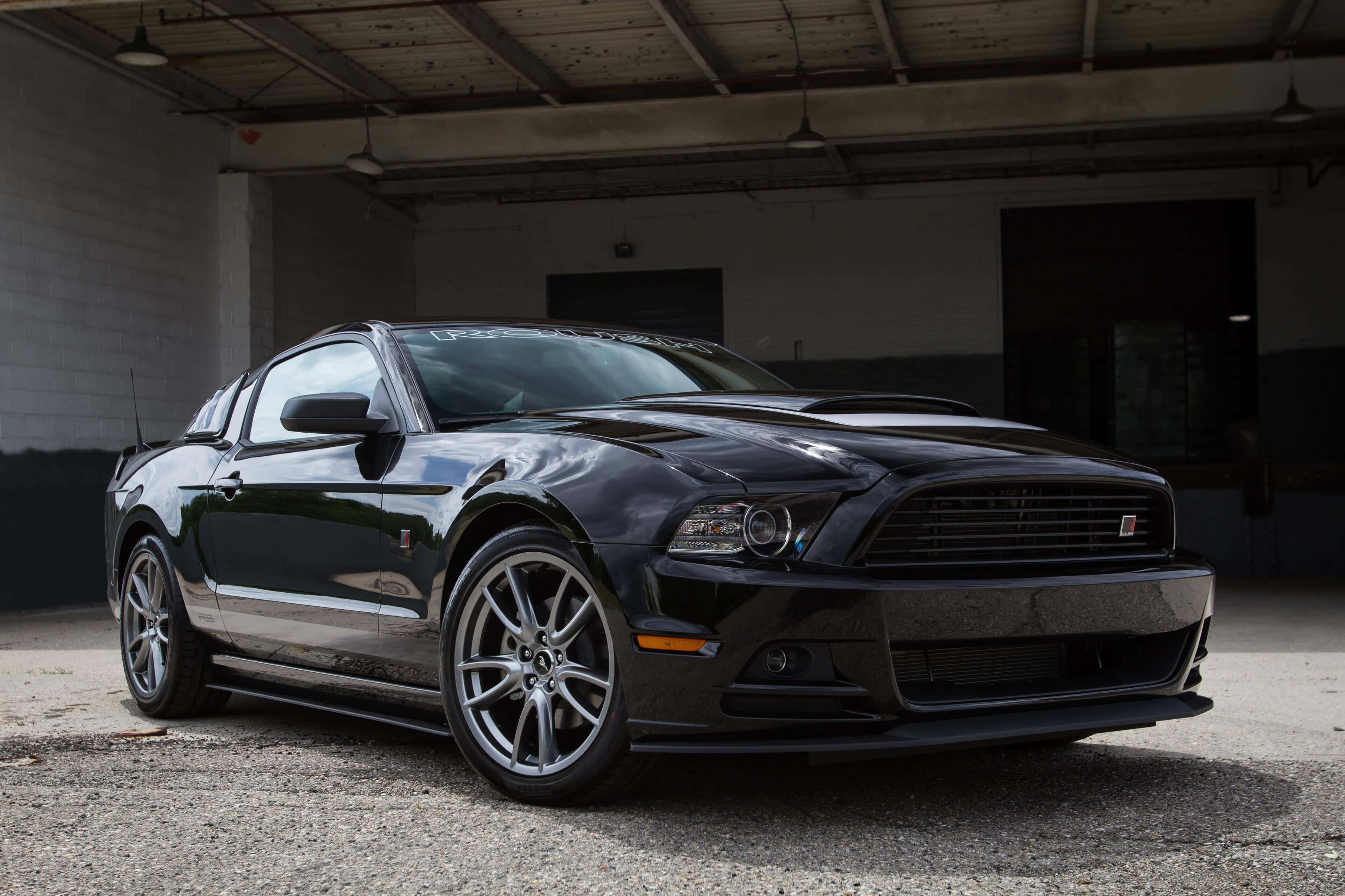 Ford Mustang Roush 桌布 壁紙 — 一輛時尚的黑色福特野馬跑車停放在燈光昏暗的工業車庫內，車庫有混凝土地板和裸露的橫樑。