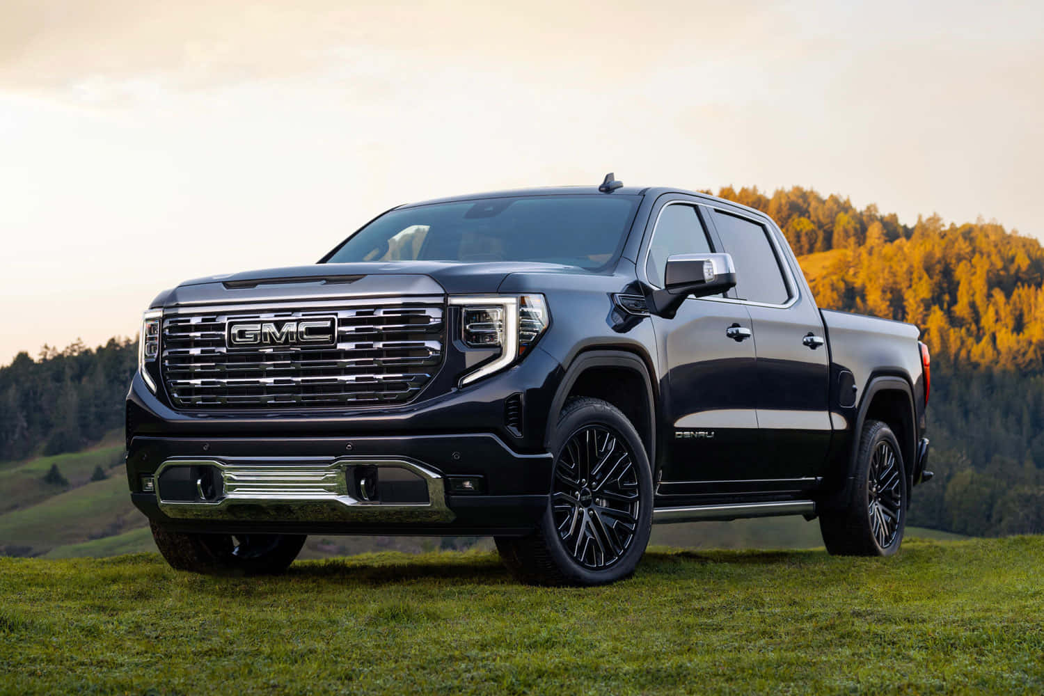 Gmc Sierra 桌布 壁紙 — 一輛時尚的黑色GMC Sierra皮卡車停在草地上，背景是金色森林山丘和柔和的日落天空。