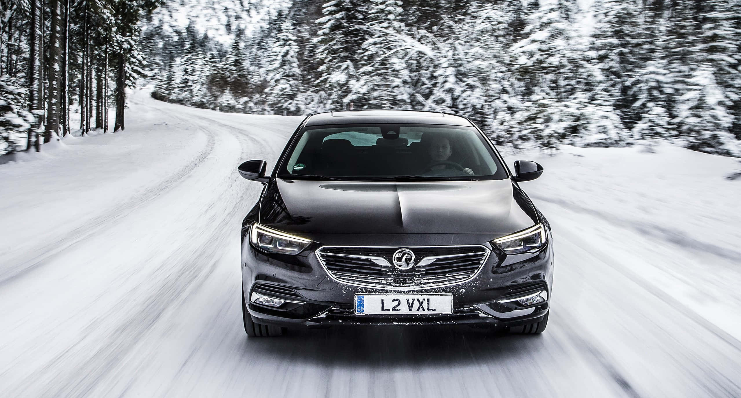Opel Insignia 桌布 壁紙 — 一輛時尚的黑色豪華轎車在白雪覆蓋的森林道路上疾馳，動態模糊強調其動態運動。